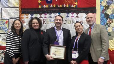 A group of doctors and staff stand in front of a quilt.