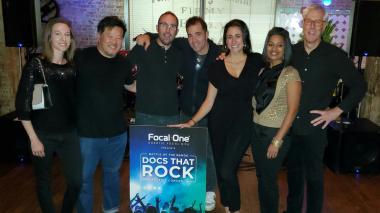 A group of participants stands around a "Docs that Rock" poster.