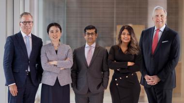 Five doctors in business dress pose for a group photo.