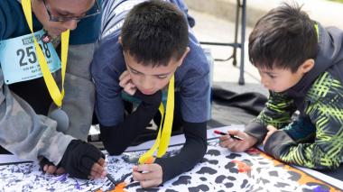 Two runners with medals on yellow ribbons examine a poster. A young sibling watches.