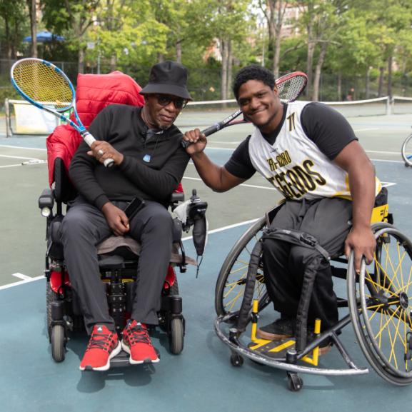 Two wheelchair athletes with tennis racquets smile for a picture.